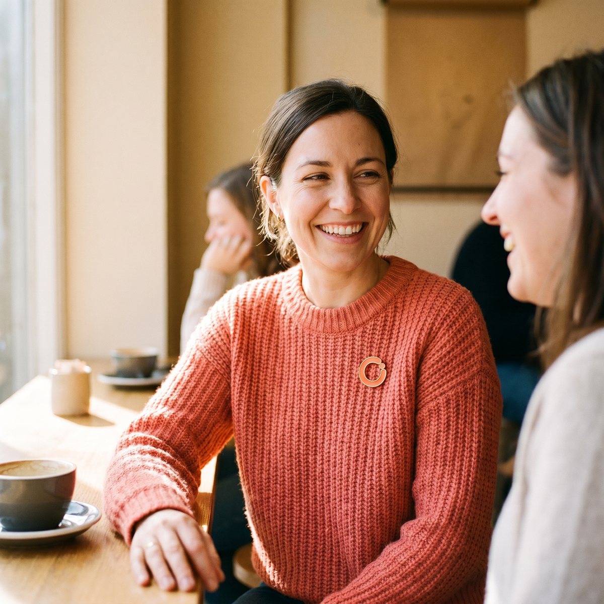 Vrouw met de koraalrode Open-speld op haar trui in een café